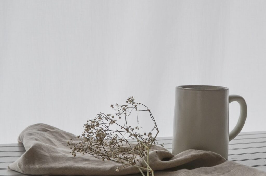 Tasse, Trockenblume und Handtuch auf einem Tisch